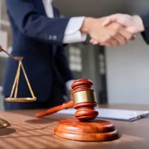 A lawyer and client shake hands featuring a gavel and scales of justice, symbolizing legal collaboration